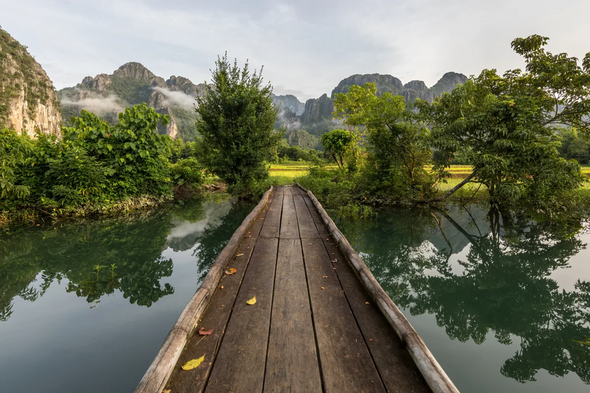 Front view of wooden footbridge over calm lagoon in the Vang Vieng landscape